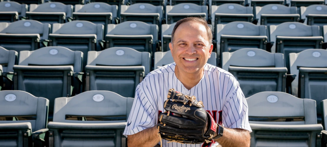 Ricardo Valerdi is seen holding a baseball glove, facing the camera and sitting in the stands