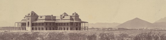 Old Main against a desert backdrop as it's being built, mountains can be seen in the background