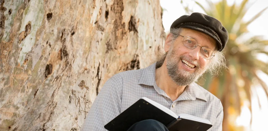 Jeff Greenberg is seen writing notes in a book and smiling at the camera