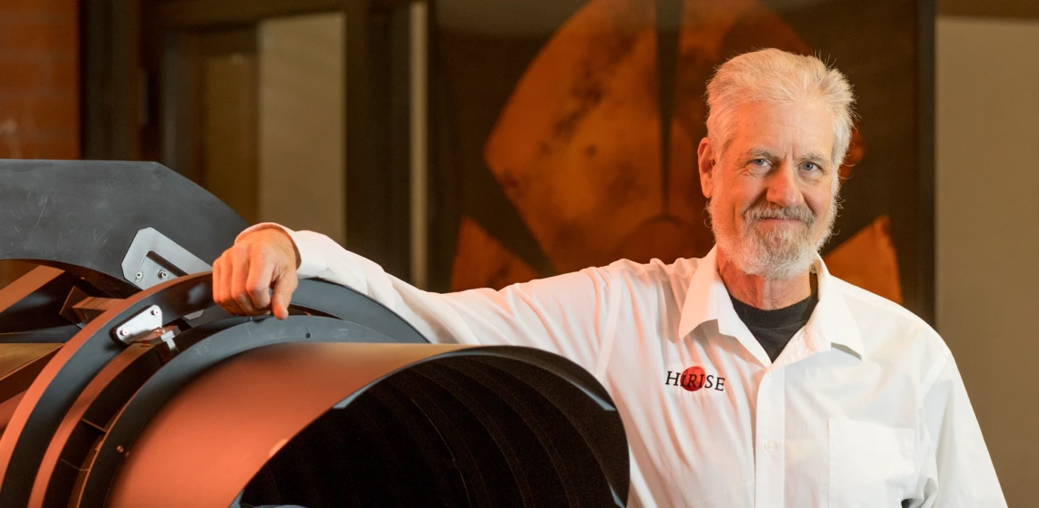 Alfred McEwen is seen posing next to a model of the HiRISE camera