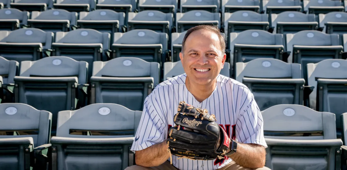 Ricardo Valerdi is seen holding a baseball glove, facing the camera and sitting in the stands